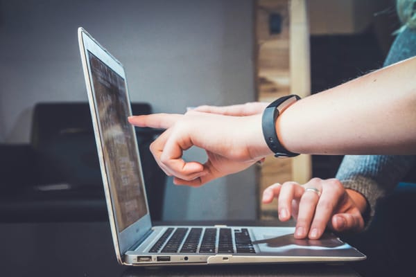 Team members work together on a laptop with two people pointing towards the screen and one controlling the mouse pad.